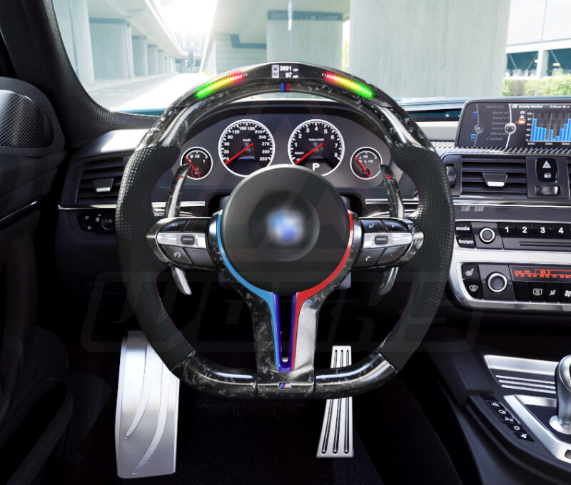 Front view of a BMW F chassis, M sport retrofit steering wheel in forged carbon fiber, extended paddle shifters, m color accents, black perforated leather, m color painted center trim, and led shift lights